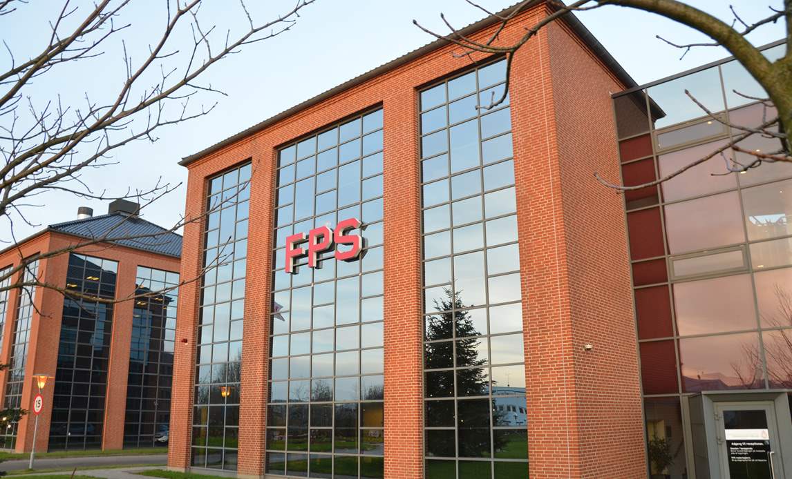 Billede af FPS hovedkontor i Ballerup - en 3-etagers rød, firkantet bygning med glasfacade hvor der står FPS med røde neonbogstaver.