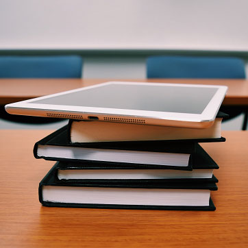 Billedet forestiller nogle skolebøger og en iPad, som ligger på et bord i et klasselokale.