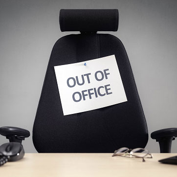 Billedet forestiller en kontorstol med et skilt påsat, hvorpå der står out of office.