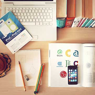 Billedet viser skriveblokke, skolebøger, mobiltelefon, laptop med videre på et skrivebord.
