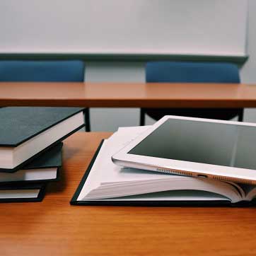 Billedet viser nogle skolebøger og en iPad på et skrivebord i et klasseværelse.